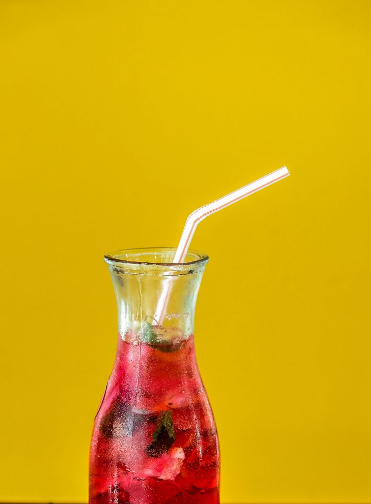 Vibrant berry cocktail with a straw on contrasting yellow background. Perfect for summer refreshment.