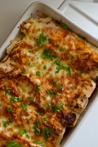 Close-up of cheesy enchiladas garnished with cilantro in a baking dish.