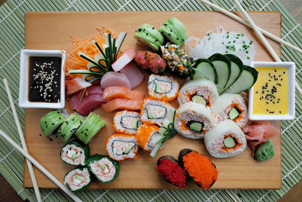 A colorful array of sushi rolls with sauces on a wooden board, perfect for food enthusiasts.