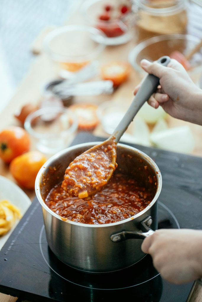 From above of crop anonymous female cook making sauce for pasta in saucepan on stove in kitchen