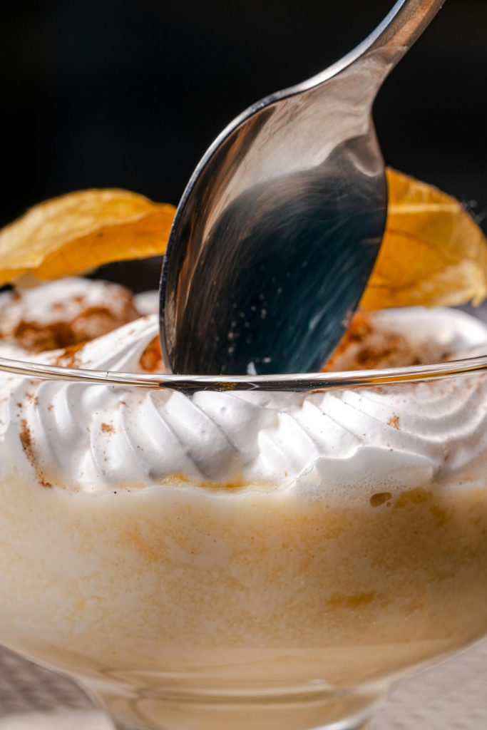 Close-up of a rich dessert topped with whipped cream and garnished, highlighting the spoon.